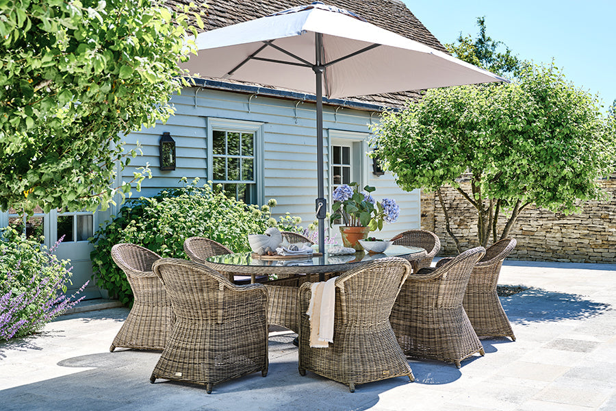Rattan garden dining set (oval dining table with eight dining armchairs) on a sunny patio with a large parasol.